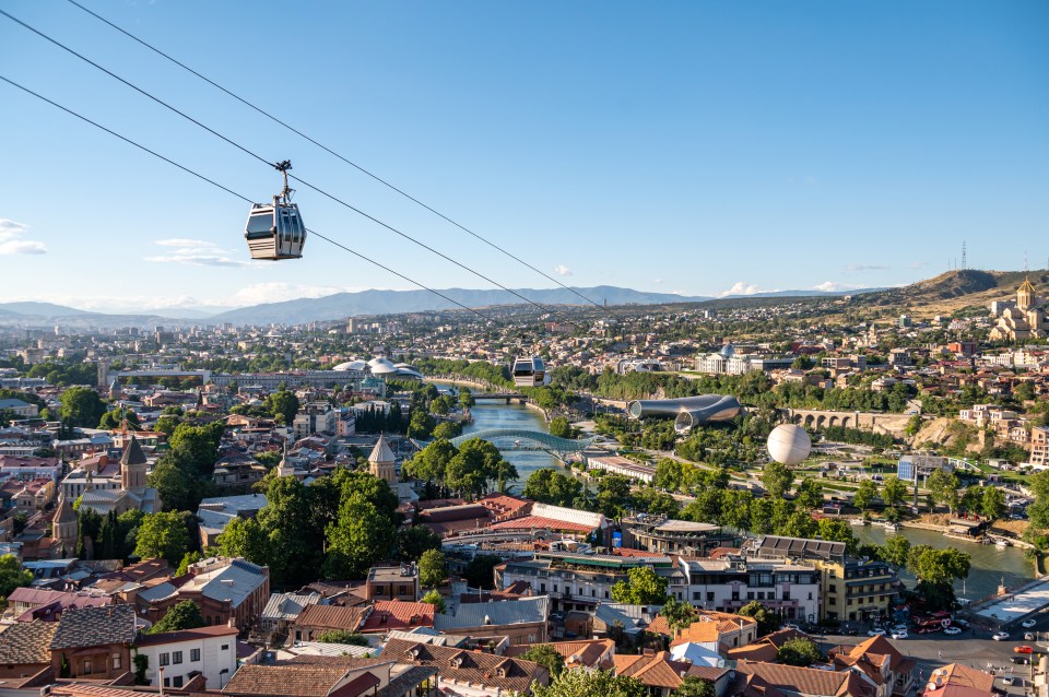 Aerial view of Tbilisi, Georgia, showing the city skyline, Kura River, and a cable car.