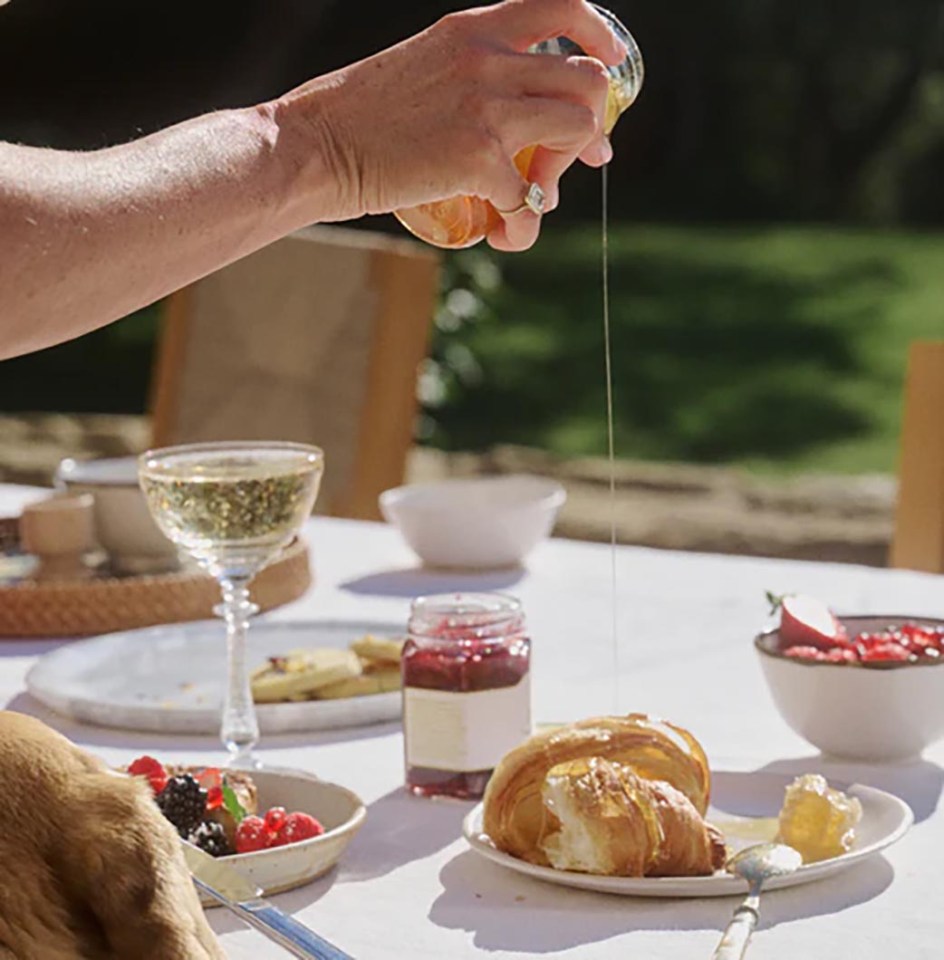 Honey being poured onto a croissant at an outdoor breakfast.