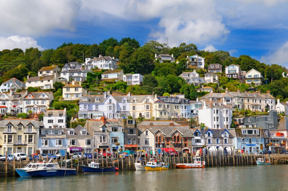Looe harbor in Cornwall, UK, with colorful houses on a hillside and boats in the harbor.