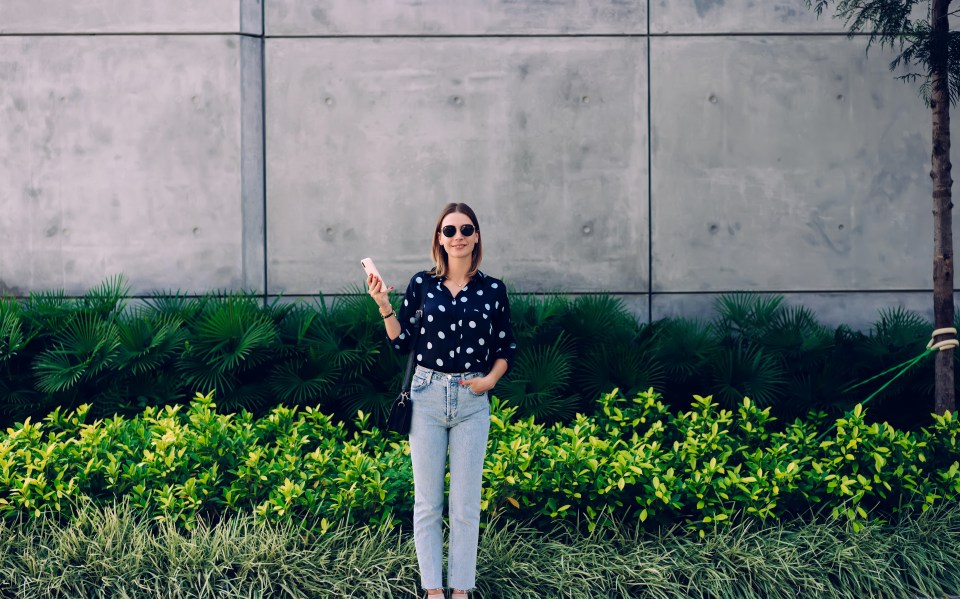 Woman standing in front of a stone wall holding a smartphone.