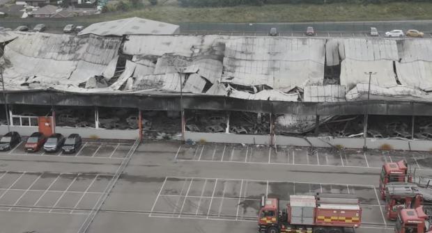 Aerial view of a fire-damaged building with collapsed roof and burned cars inside.