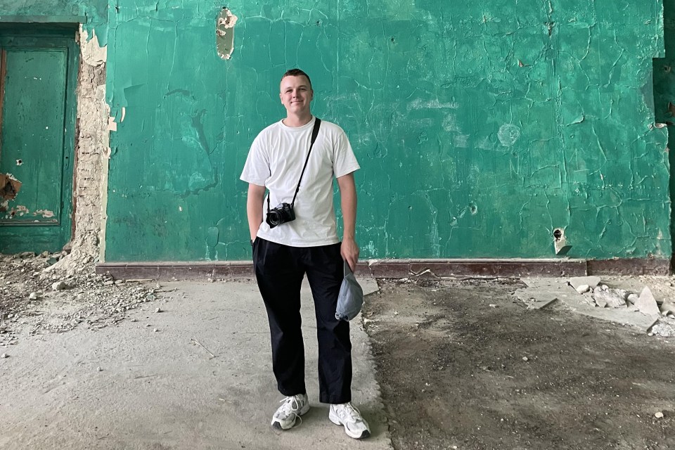 A photographer stands in a dilapidated building with peeling green paint.