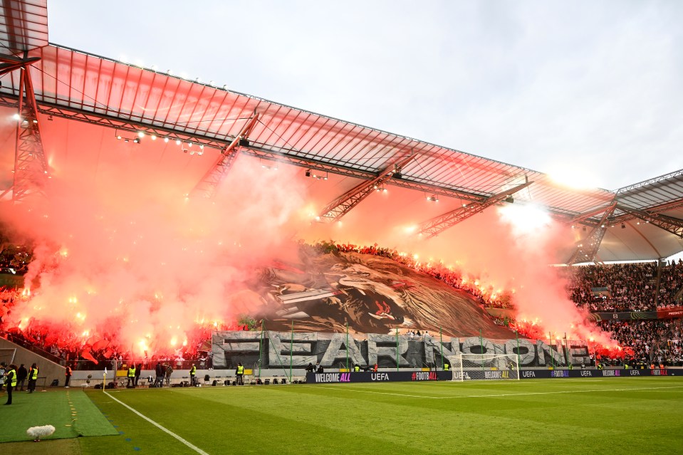 Legia Warsaw fans lighting flares in a stadium.