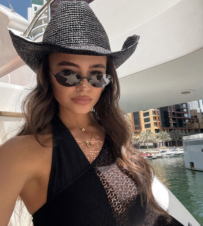 Natalya Wright on a yacht in Dubai wearing a black cowboy hat, sunglasses, and a black halter top.