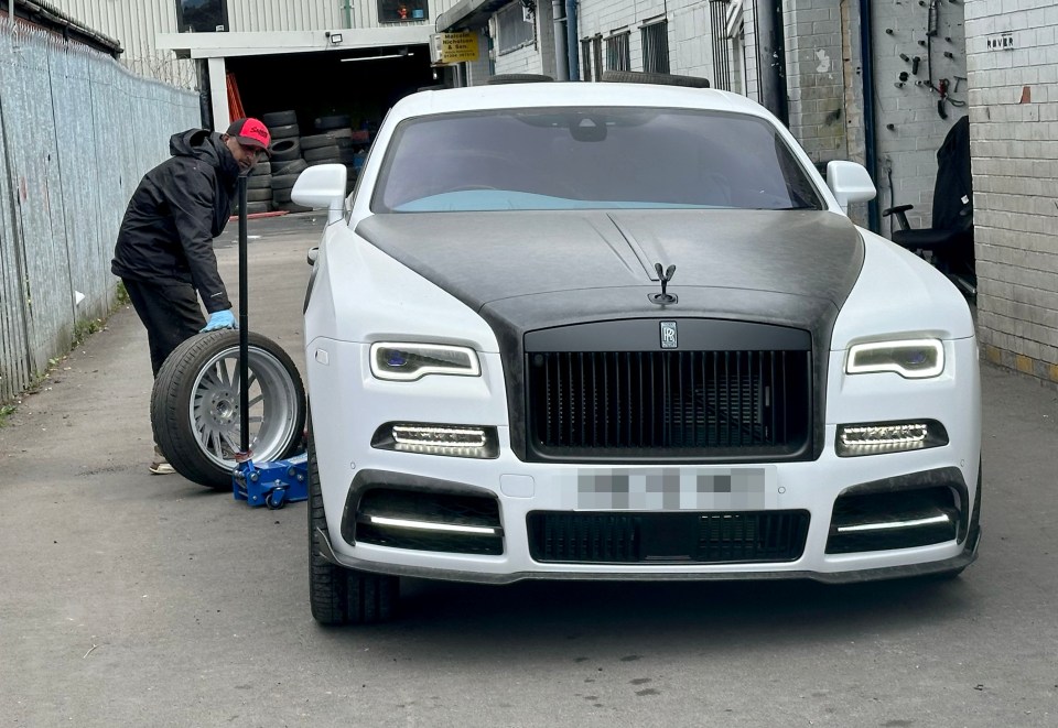 A man changing a tire on a Rolls Royce.