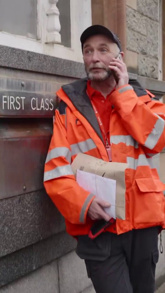 Postman on a phone call by a first-class postbox.