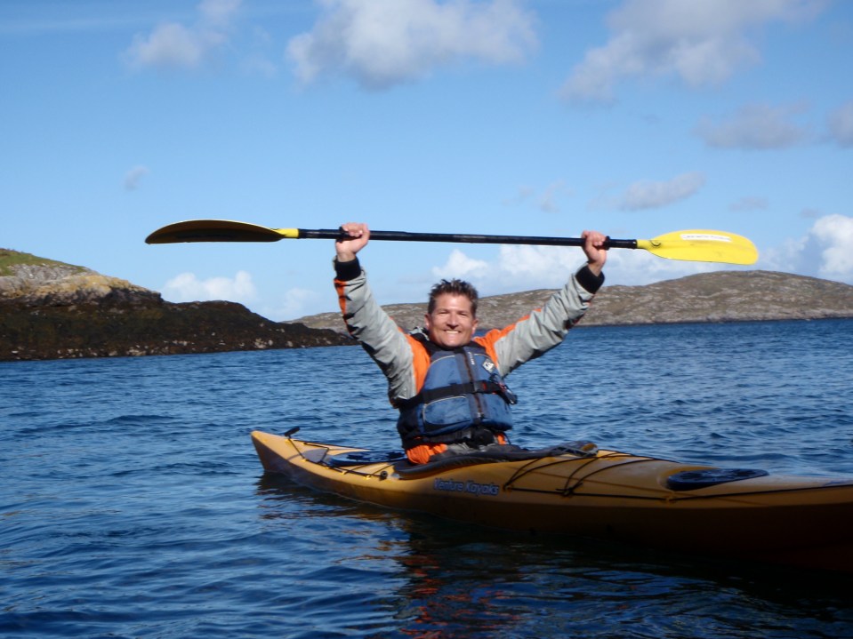 Man celebrating in a kayak with paddle raised.