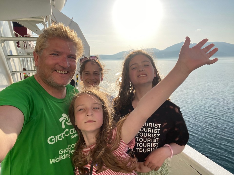 Family selfie on a ferry, overlooking the sea and mountains.