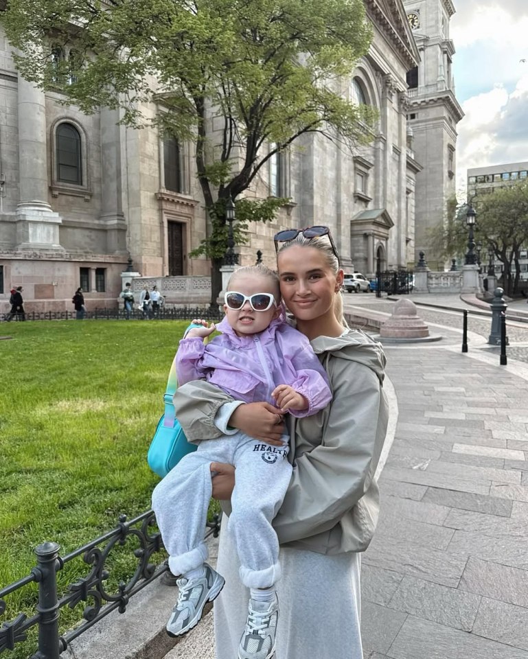 Woman holding toddler in front of a church.