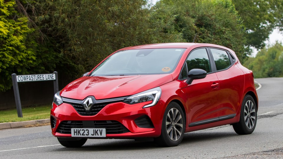 Red Renault Clio driving on a road.