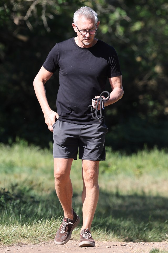 Gary Lineker walking in a park, holding a dog leash.