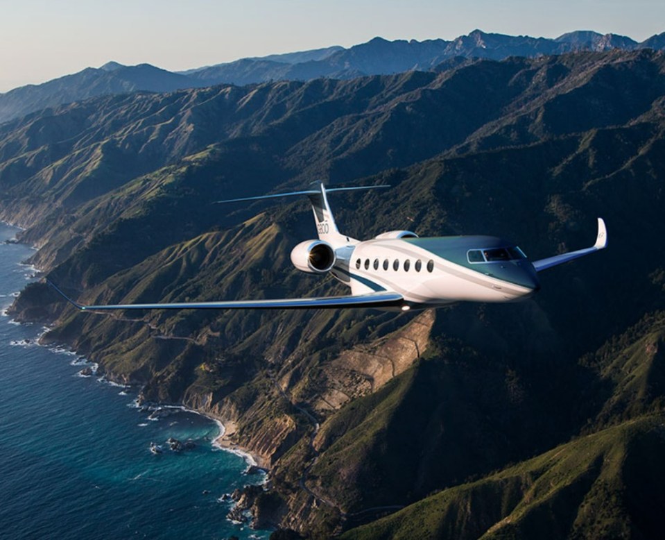 Private jet flying over mountains and ocean.