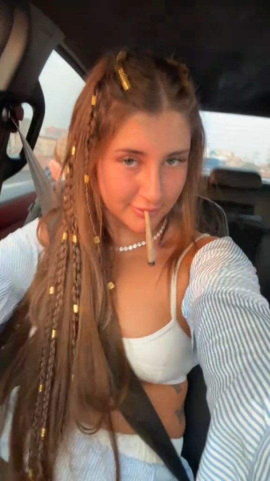 Selfie of a young woman with long braided hair holding a joint.
