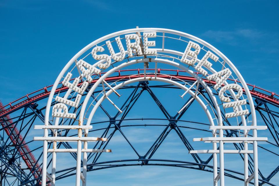 Blackpool Pleasure Beach entrance sign with roller coaster in background.