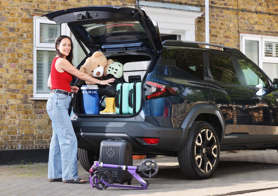 A woman packing a car's trunk with luggage, a teddy bear, and other items.