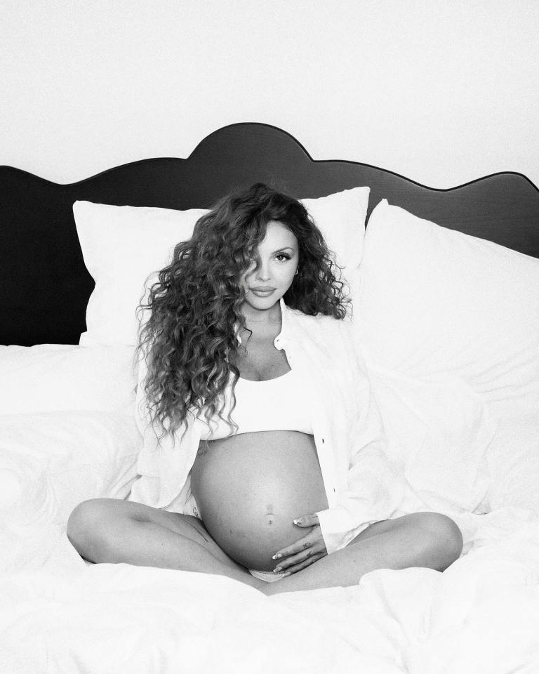 Black and white photo of a pregnant woman sitting on a bed.