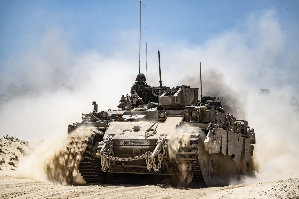 Israeli army tank moving along the border, kicking up dust.