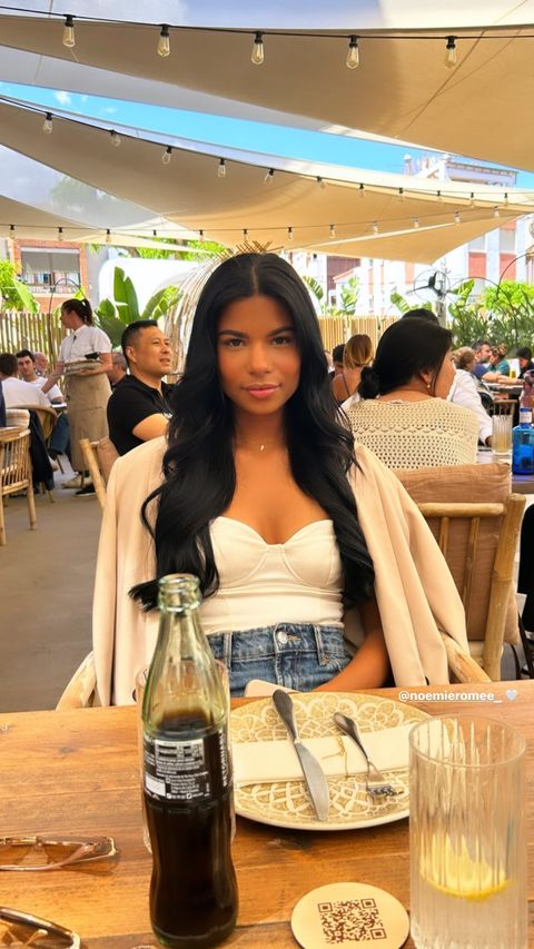 Woman with long black hair sitting at an outdoor restaurant table.