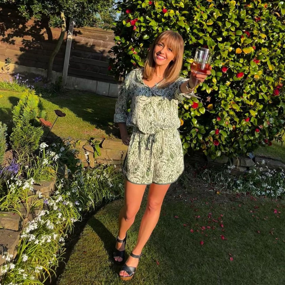 Woman in a green jumpsuit toasting with a drink in a garden.