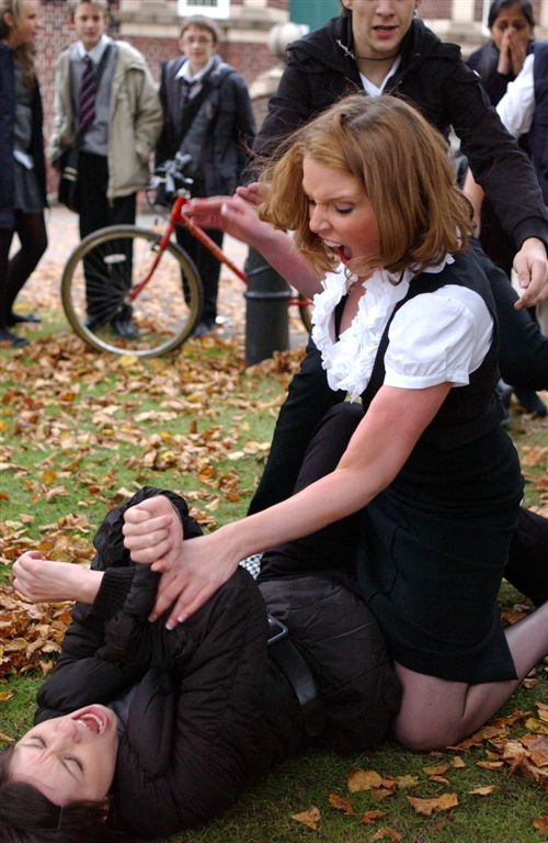 Two women fighting on the ground amidst fallen leaves.
