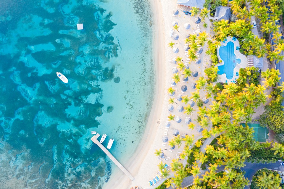 Aerial view of a resort beach with swimming pool, palm trees, and beach umbrellas.