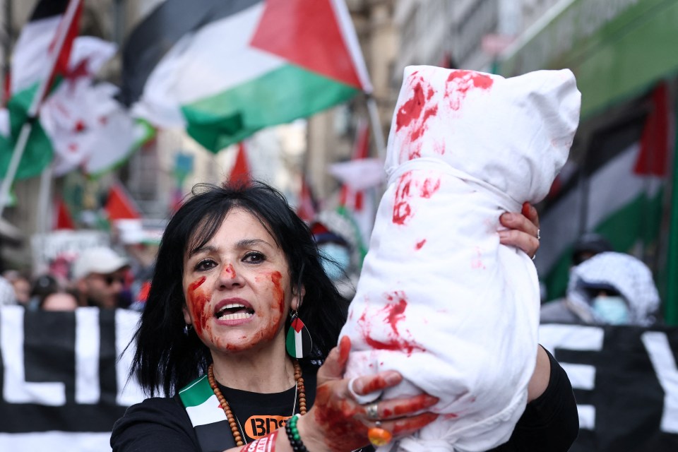Woman at a pro-Palestinian protest holding a prop body bag stained with red paint.