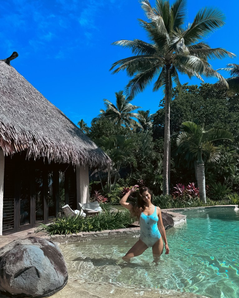 Woman in a light blue swimsuit standing in a tropical pool.