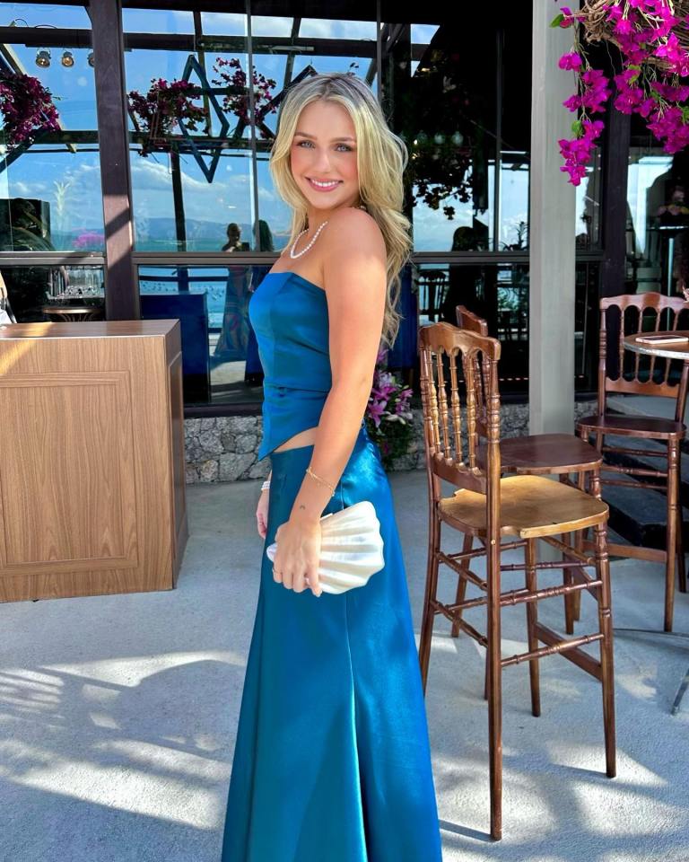 Woman in teal dress holding a white clutch.