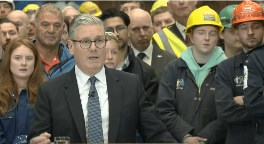 Man in suit speaking to a crowd of workers.
