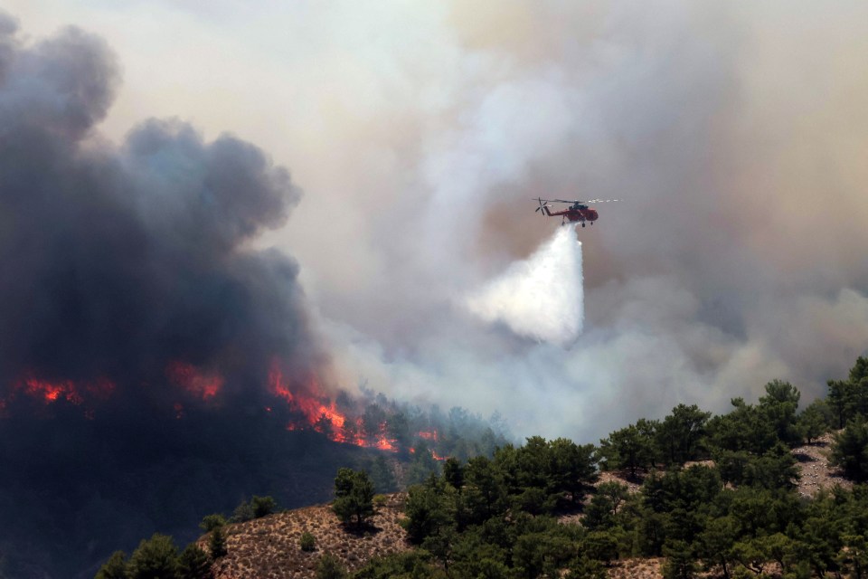 A firefighting helicopter drops water as a wildfire burns near the village of Archangelos