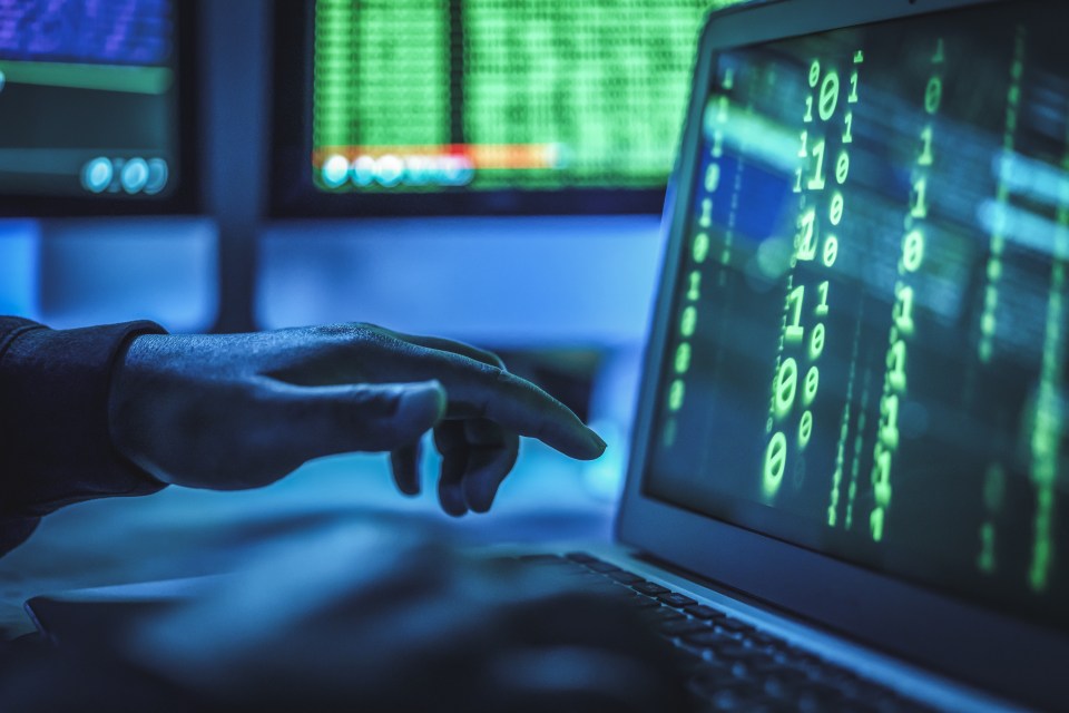 Person's hand hovering over a laptop displaying binary code.