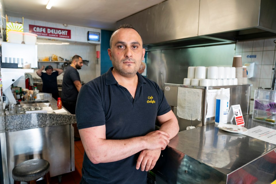 a man in a cafe delight shirt stands in front of a counter