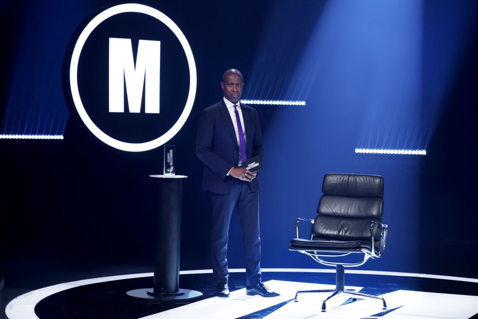 a man in a suit and tie stands in front of a large letter m