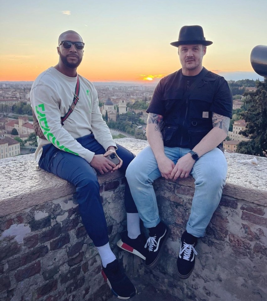 two men sitting on a ledge with one wearing a shirt that says ' lmc ' on it