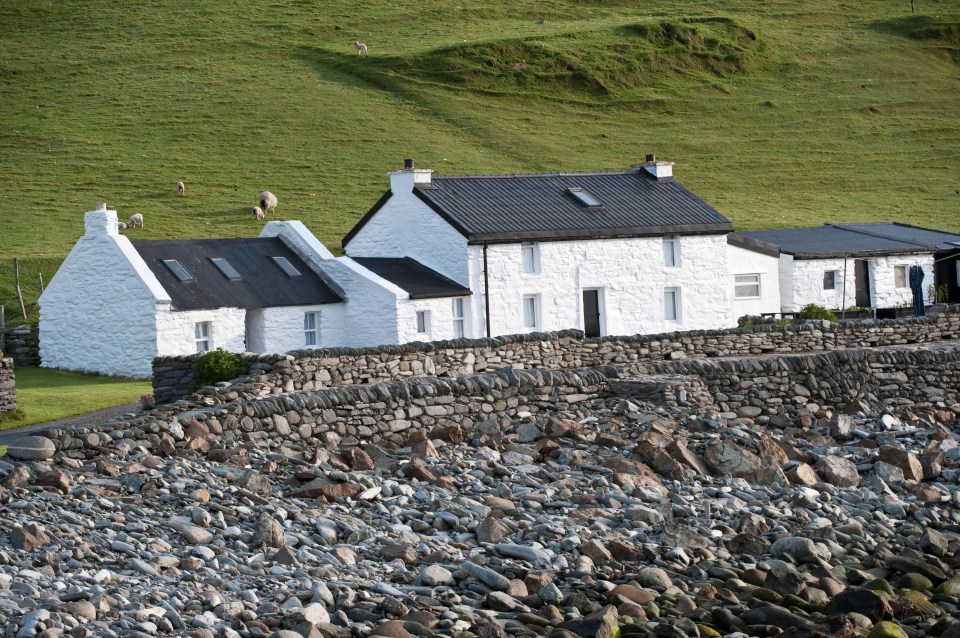 a white house with a black roof sits next to a stone wall