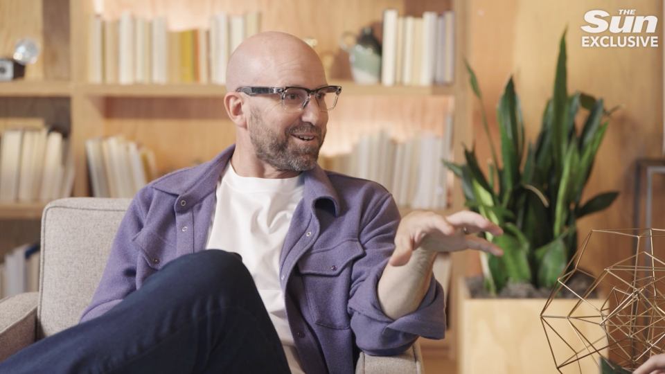a man wearing glasses sits in a chair with the sun exclusive written on the bottom