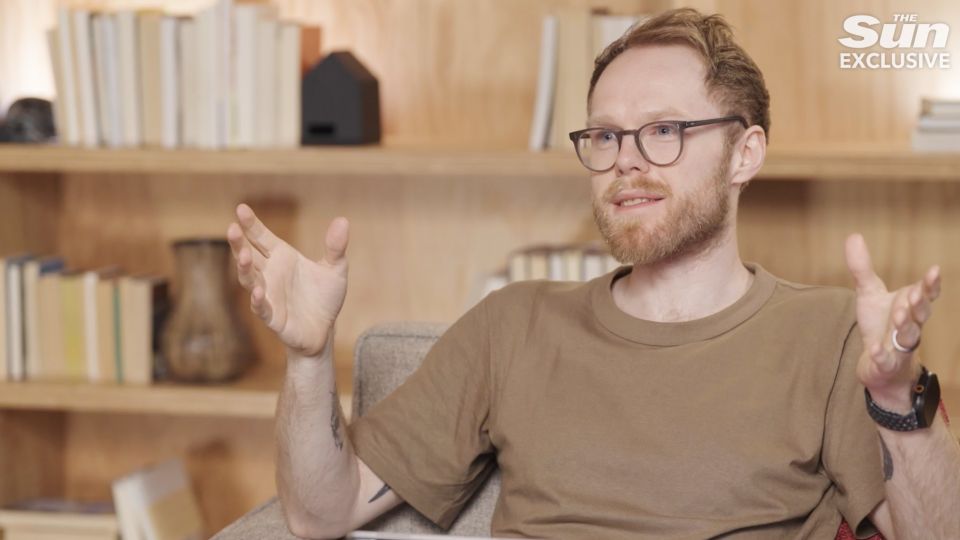 a man wearing glasses is sitting in front of a bookshelf with the sun exclusive written on the bottom