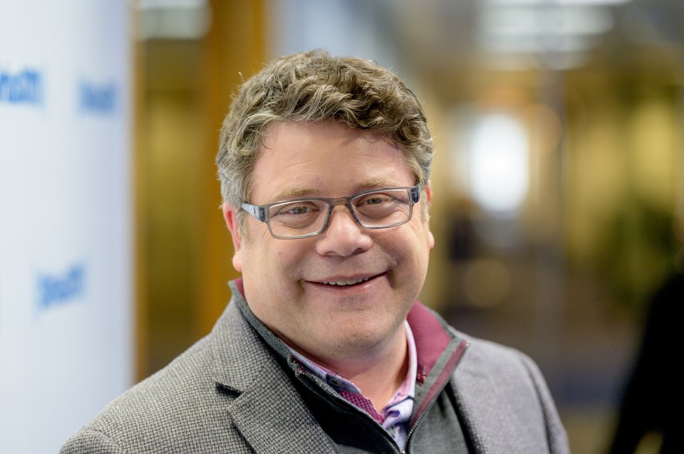a man wearing glasses and a suit smiles for the camera