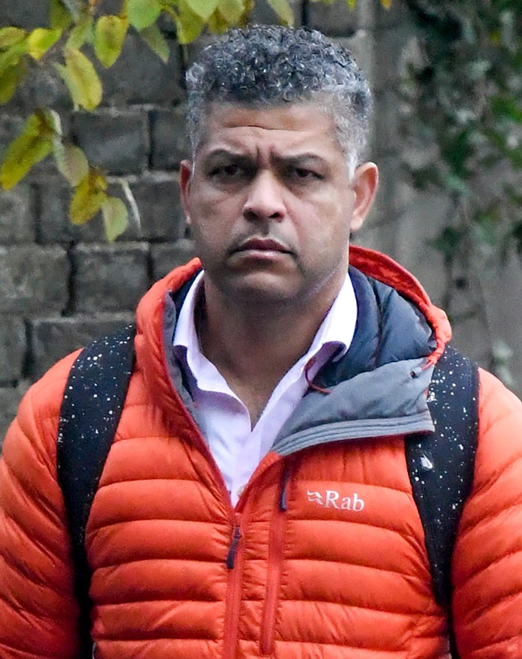 a man wearing an orange rab jacket stands in front of a brick wall