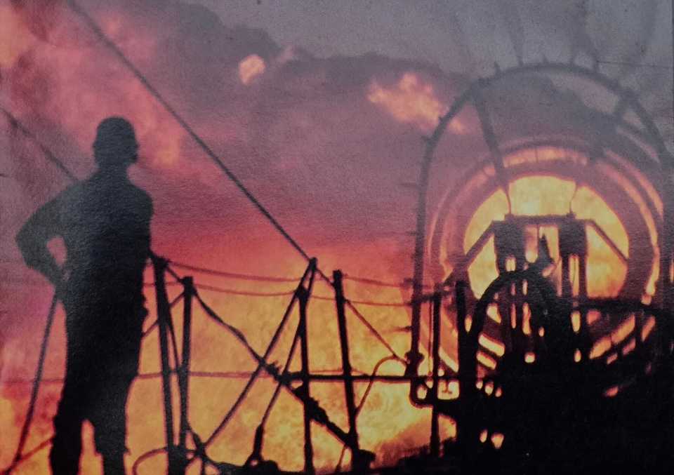 a man in a hard hat stands in front of a large fire