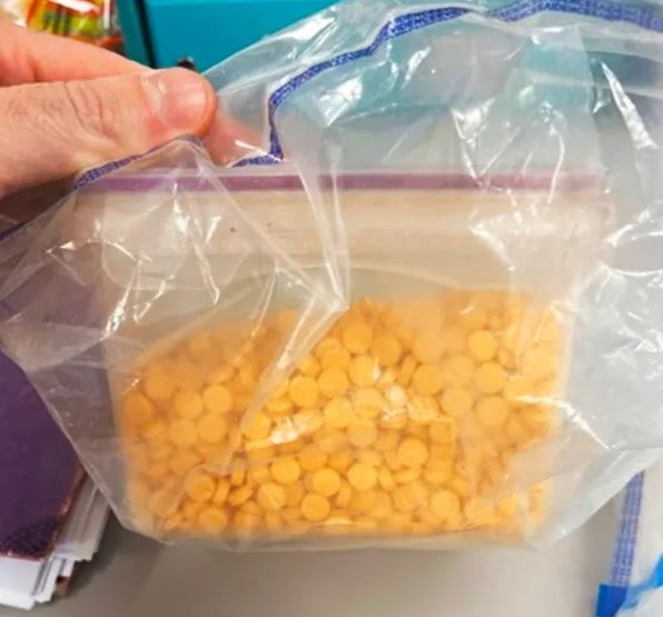 a person is holding a plastic bag filled with yellow pills .
