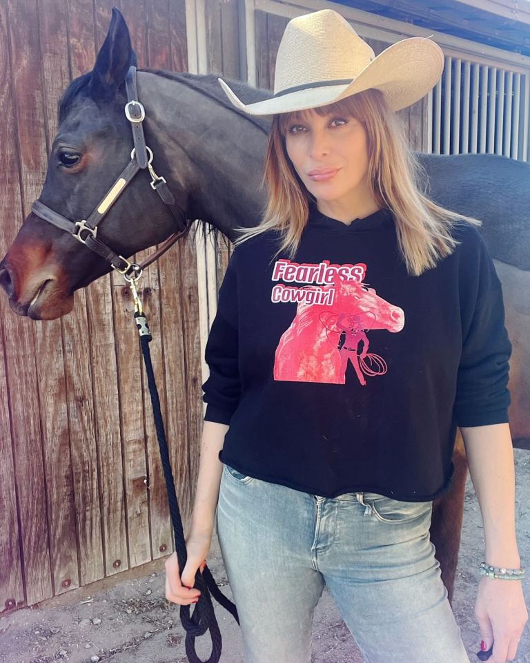 a woman wearing a fearless cowgirl sweatshirt stands next to a horse