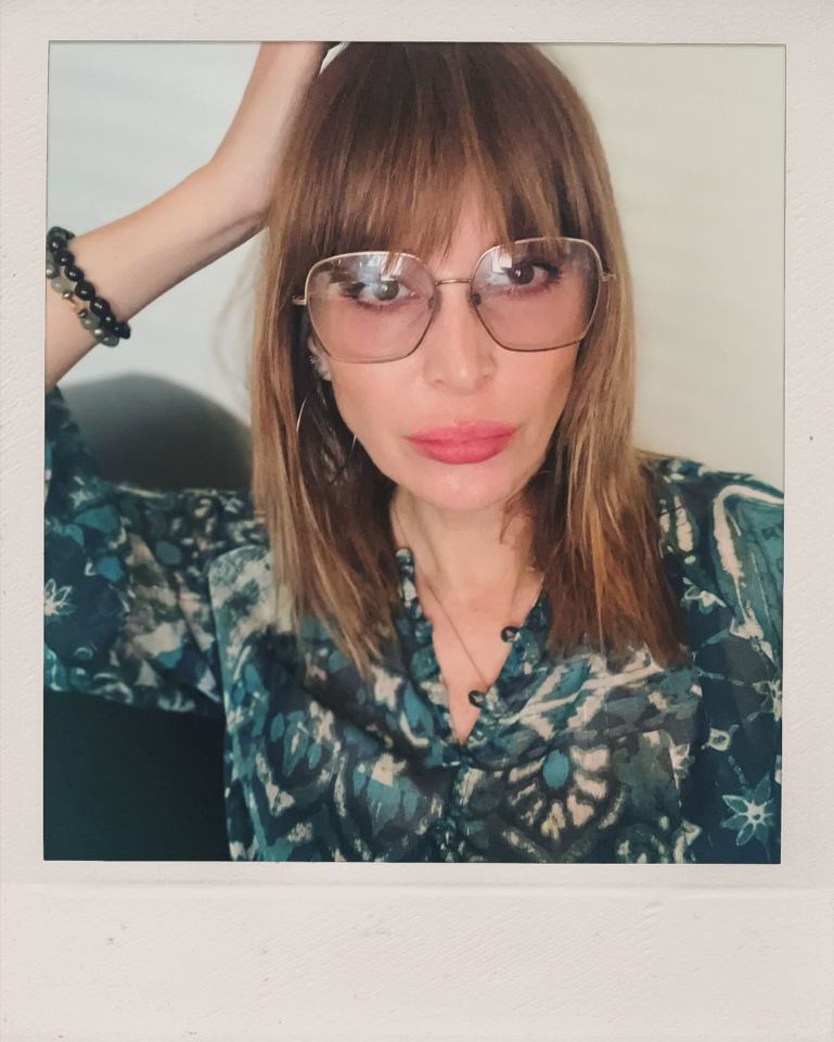 a woman wearing glasses and a blue shirt has her hand on her head