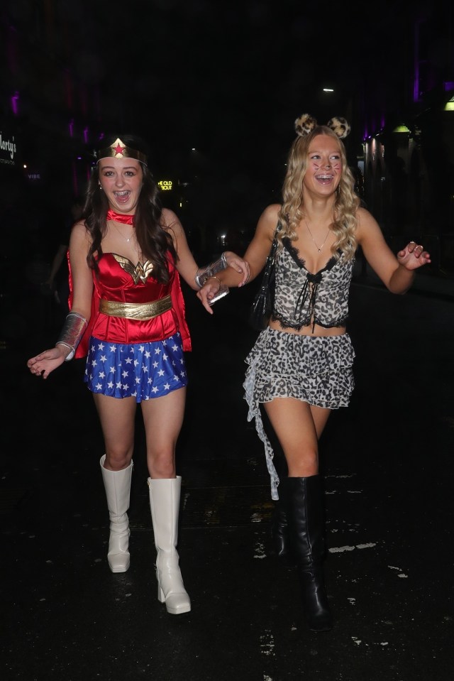 Two women in fancy dress costumes walking down the street at night.