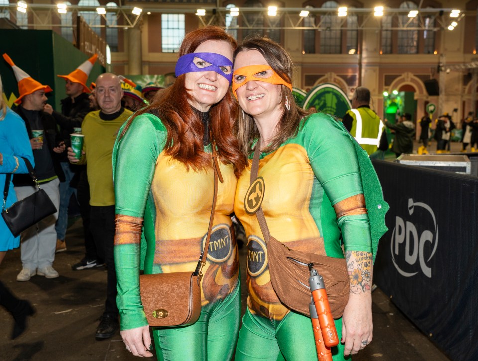 Two women dressed as Teenage Mutant Ninja Turtles at a darts event.