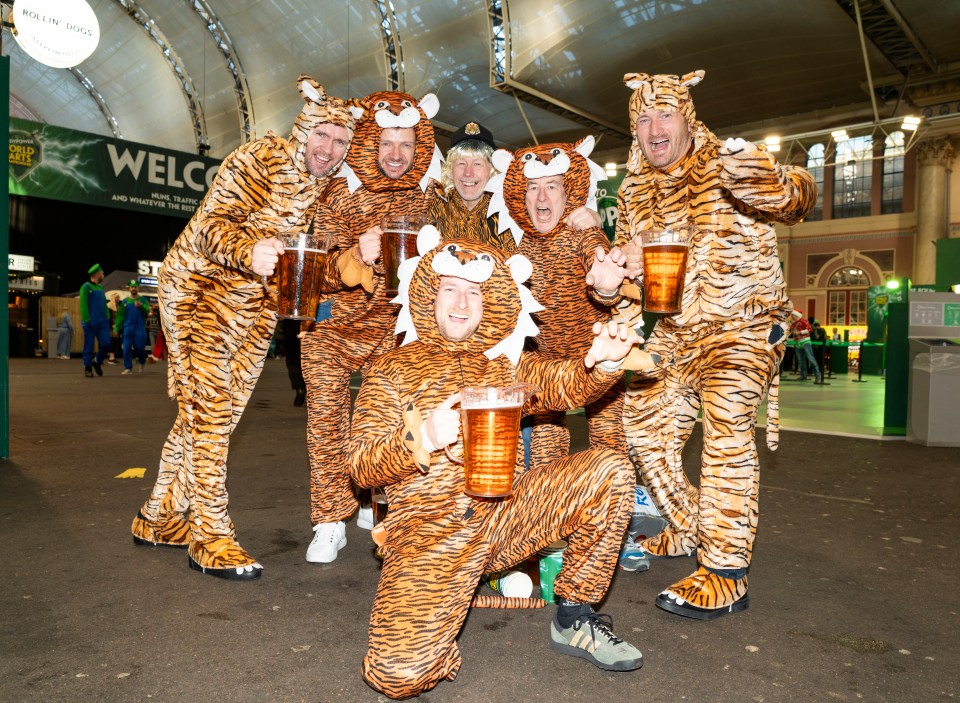 Group of men in tiger costumes holding large beers at a darts event.