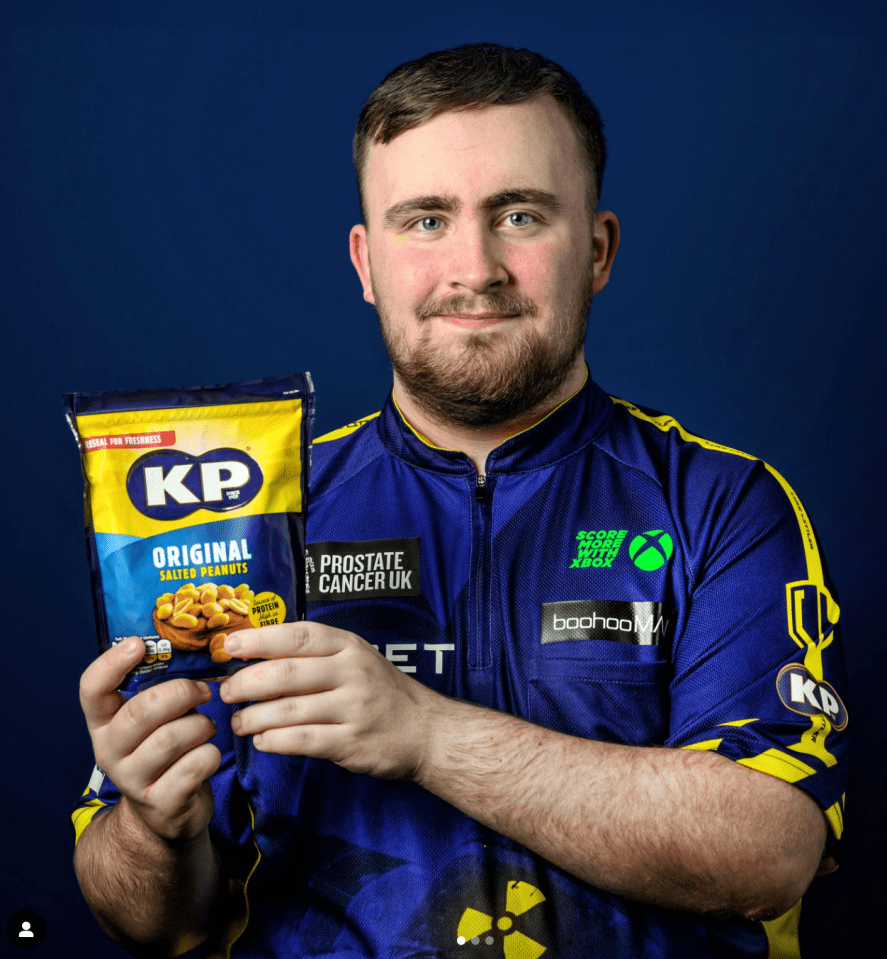 Man holding bag of KP salted peanuts, wearing a jersey supporting Prostate Cancer UK.
