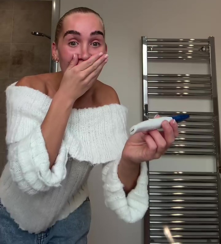 Woman in white sweater reveals positive pregnancy test.