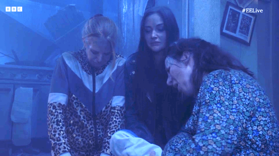 Screenshot of three women comforting each other in a dimly lit room.