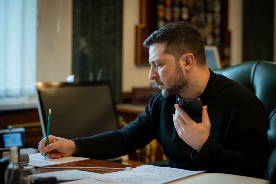 Volodymyr Zelenskyy writing and holding a phone.